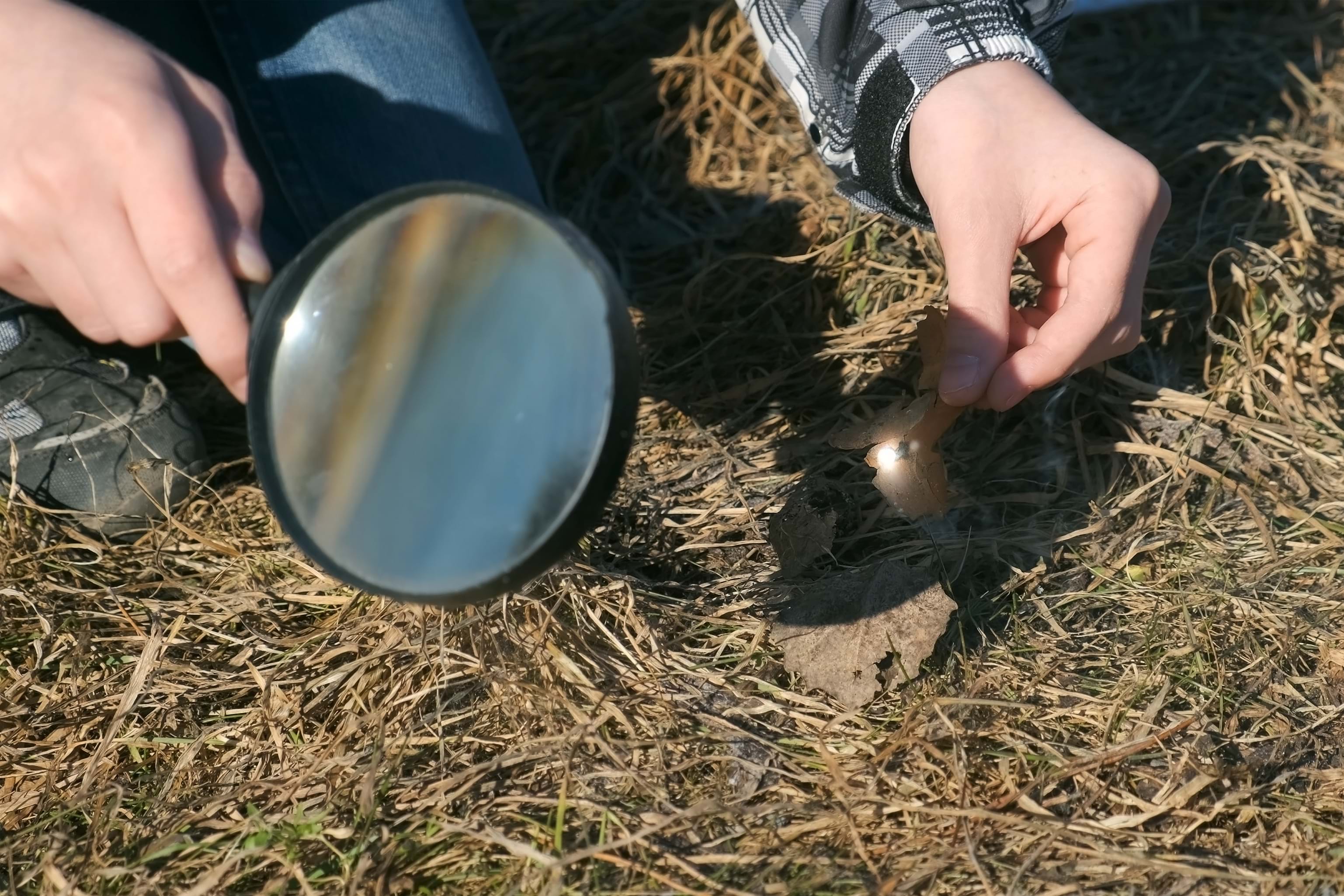 Hånden til en gutt med et forstørrelsesglass som prøver å sette fyr på gresset i gata. Barneeksperimenter i naturen. Solstrålene passerer gjennom forstørrelsesglasset og skaper ild.